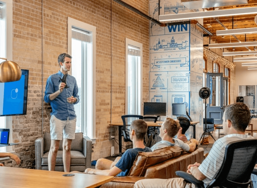A man presenting his project design ideas while his colleagues  sit in front listening.